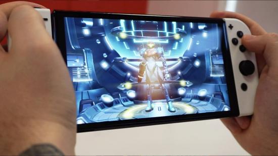 A pair of hands hold the Nintendo Switch OLED model, while Samus from Metroid Dread stands confidently in centre frame