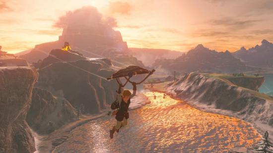 Link glides away from a cliff, over a lake lit beautifully by the setting sun. The landscape is lit up a glowing red colour