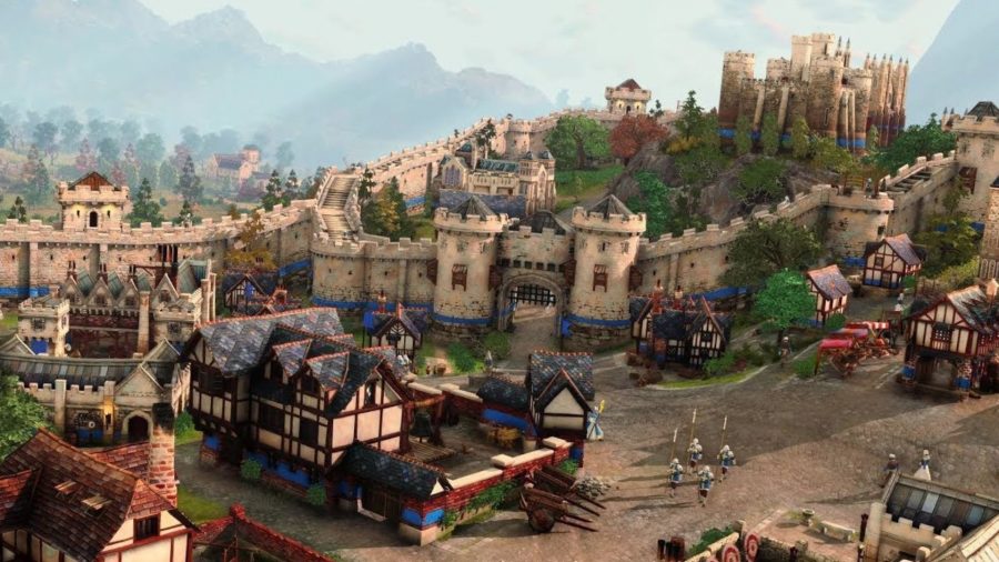 A scene from Age of Empires, showing a castle settlement, with various battlements and old buildings, foliage dotting pathways, and tiny figures walking around.