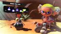 A ponytail-esque Splatoon 3 hairstyle. Shown off by a character with grey shoes, yellow hair, sat in the desert with a cliff face behind them,and a small cute fish creature with an orange tuft of hair coming out the top of their head, and the menu options for choosing the hairstyle above.