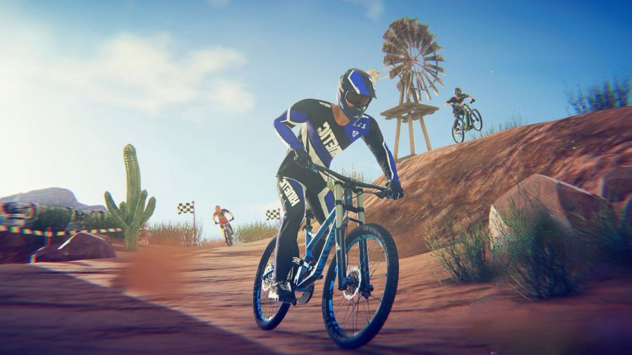 Art for our Descenders mobile review showing a biker riding towards the camera along a dirt path with banked dirty bits either side. There is a wooden mill in the background, along with a blue sky and a single cloud. There are also a couple of cactuses in the back.