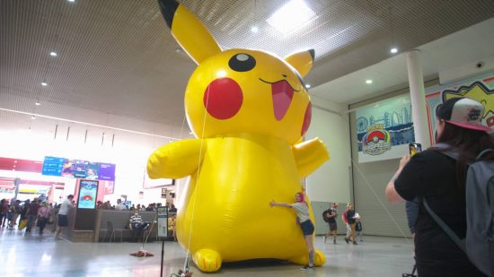 Pokemon Worlds 2022: a large inflatable Pikachu is visible in the middle of a wide corridor, being hugged by a fan with cool hair