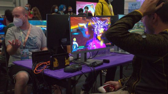 Pokemon Worlds 2022: two players sit on chair opposite each other, playing the fighting game Pokken