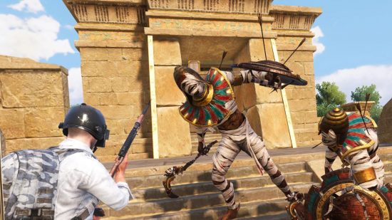 A man in a helmet, white shirt, with a silver rucksack and an AK47 faces up to a living mummy, with paper wrapped around their limbs and face, a shield pierced with arrows, and a hooked weapon in their hand in a screenshot from PUBG mobile.