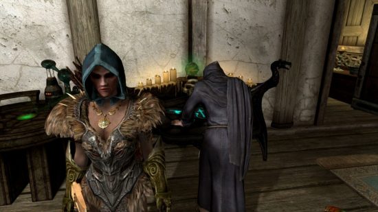 A woman in a hood and fur armour stands in front of a man standing over a glowing countertop enchanting an item, for our Skyrim enchanting guide.