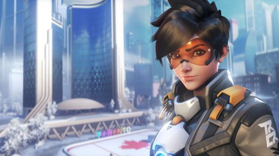 Tracer, and Overwatch 2 characters, standing in front of a cityscape background. They have short black hair, orange goggles, and a white and black outfit.
