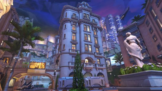 An Overwatch 2 map showing a scene showing a tall apartment building with trees below and other skyscrapers rising up behind.