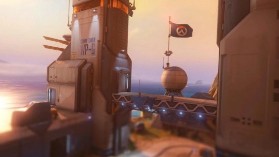 An Overwatch 2 map showing a scene showing a military building by the coast at sunset.