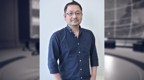 Yosuke Saito, producer of Nier Automata, wearing a blue shirt. He has short black hair and glasses and his hands in his pockets.