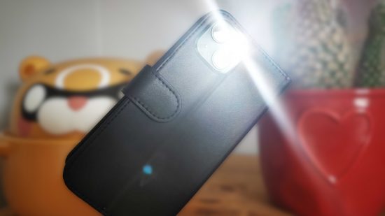 An iPhone with the flashlight on leaning against a red pot