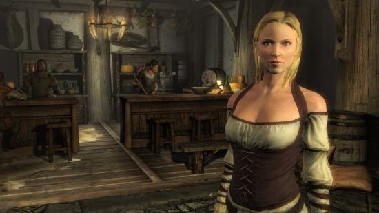 Skyrim potion recipes: a blonde woman stands in a shop in the foreground with another sweeping in the background behind a wooden counter in a screenshot from Skyrim.