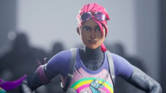 Fortnite iPhone - a woman with pink hair, sunglasses on her forehead, a colourful top and arms on her hips looking forward in a screenshot from a Fortnite video.