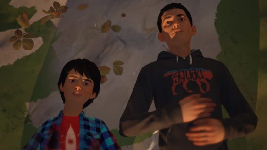 Life is Strange 2 review: Sean and Daniel Diaz, two Hispanic young boys, laying next to each other on a grey rock dapled with autumn leaves. Sean is on the right and wears a black hoodie with a red picture of a wolf that says 'squad', and Daniel wears a blue plaid shirt stained with fake blood over a red tshirt with a rocket on it.