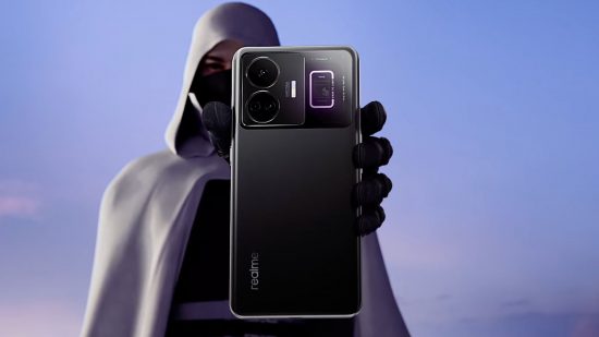 Android 240W charging - a man in a hooded grey cloak and a mask holds out a black phone in front of his face, showing its back to the camera.