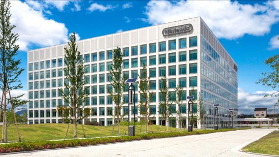 Nintendo pay rise news - header showing a large cuboid building on by grass with thin trees near it, below a lightly clouded blue sky. The building is white with a grid of close-together windows and the Nintendo logo in the top right corner.