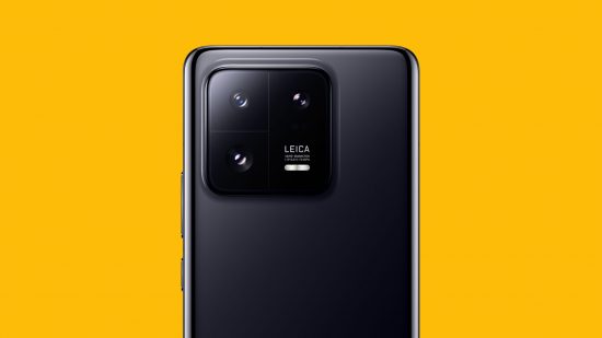 The Xiaomi 13 Pro on a mango yellow background, showing us the top back of the phone, its three cameras with Leica branding and slightly curved edges.