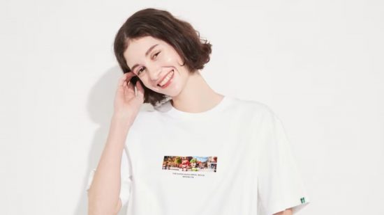 A woman with a brown bob in a Mario movie Uniqlo t-shirt. It's white with a screenshot small in the middle. She is tilting her head to her right and touching her hair with her right hand.