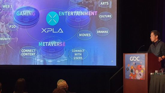 Summoner's War Web3 GDC talk with Kyu Lee on the right by a speakers podium looking at a slide with words like 'metaverse' on it, all blue.