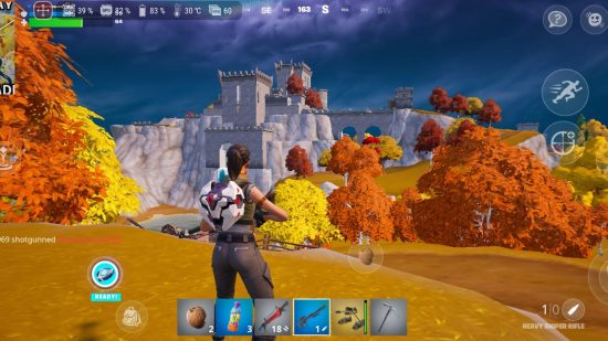 Asus ROG Phone 7 review - a screenshot from Fortnite, a third person shooter, showing a woman with a backpack standing on yellow grass in front of autumnal trees and a castle built into a cliff face.