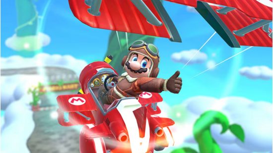 Gry mobilne Mario — Mario w gokarcie szybującym w powietrzu w starym kostiumie lotniczym.  Gokart jest czerwony, szybowiec jest czerwony, a rozmyte tło ma dużo chmur.