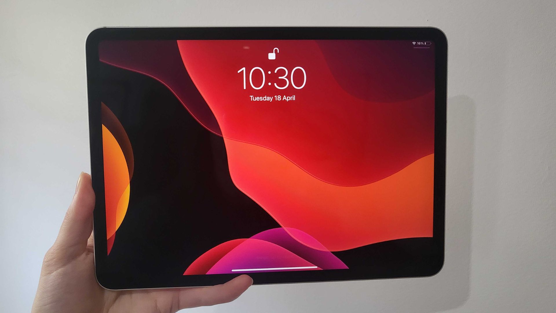 One of the best portable gaming consoles -- an iPad Pro. It is a large square screen with thin black bezels, a time in the middle at the top showing 10:30 and a red and black background. A hand is holding it in the bottom left corner. Behind is a white wall.