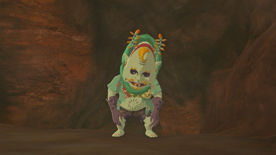 Zelda: Tears of the Kingdom bubbul gems -- Koltin, a monster with a large head, green skin, purple gloves, and colourful headwear walking out of a cave looking despondent. The cave walls are sandy red or brown.