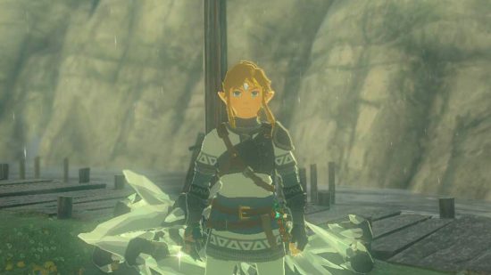 Zelda: Tears of the Kingdom glitch -- Link, a blonde boy in white armor wearing a diamond circlet standing in front of a wooden pole standing vertically, in front of a stony mountain face. On the ground behind him is a pile of oversized diamonds.