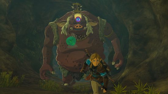Zelda: Tears of the Kingdom update - Link, a bold boy in a blue tunic with weapons on his back running towards the camera through a dark cave away from a large one-eyed beast. The monster's skin is red, his eye glows yellow, he is about five times the size of Link with a big belly and a pale red nose.