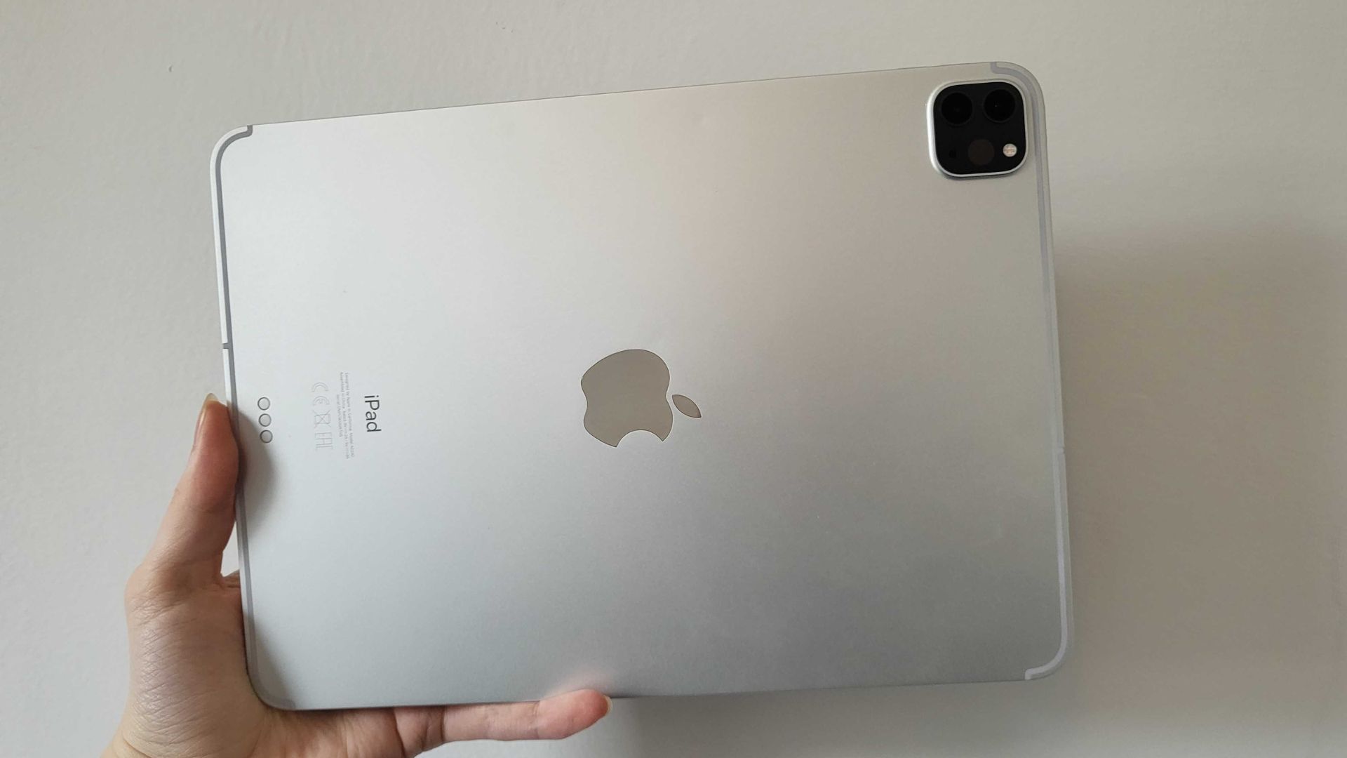 Jeden z najlepszych iPadów, iPad Pro, w kolorze srebrnym, trzymany w lewym dolnym rogu, na boku, pokazując srebrny tył, czarny aparat w prawym górnym rogu i logo Apple pośrodku.