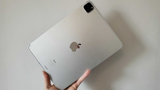 One of the best iPads, the iPad Pro, in silver, held in the bottom left corner, on its side, showing its silver back, black camera in the top right, and apple logo in the middle.