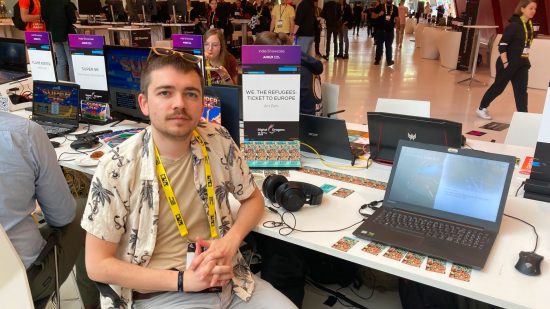 We The Refugees Ticket to Europe interview: Photo of a white man wearing a yellow lanyard sat next to a laptop in an expo hall