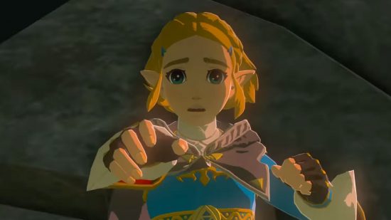 Zelda Tears of the Kingdom depths - Link, a blonde boy in a blue tunic, leaping through the air and falling rocks reaching out his hand to Zelda, a blonde woman in a blue tunic and black gown. The shot is a closeup on Zelda's face.