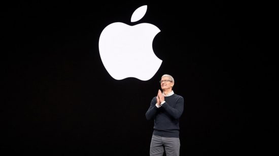 Apple logo trademark in white, an Apple with a bite out of it, above Tim Cooke a grey haired man in smart clothes with hands clasped together, all on a black background.