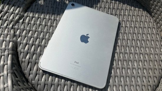 iPad 10 gen review - the iPad in silver lay on its screen on a wood surface. We see its back, showing the Apple logo in the centre and small single camera ring in the top right corner.