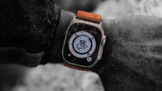 Apple Watch Ultra 2 release date header showing a large smartwatch on a man's wrist. Everything is in black and white except for the watch, which has a white compass on its screen, silver casing, and a bright orange strap.