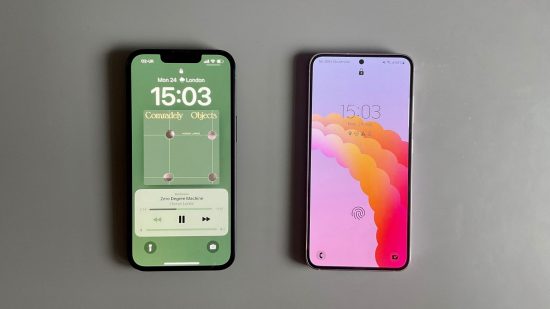 iPhone vs Android header showing an iPhone 14 in black and a Samsung Galaxy S23 in lavender. Both are face up, with the iPhone on the Lock Screen with some music playing, showing the artwork which is mostly a pale green shade. On the right the Samsung is also locked, with an abstract pink and purple background.