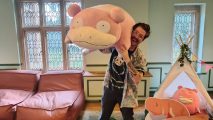 Pokémon Sleep review: an excuted man covered in tattoos and wearing a jazzy shirt holds up a giant slowpoke plush while smiling