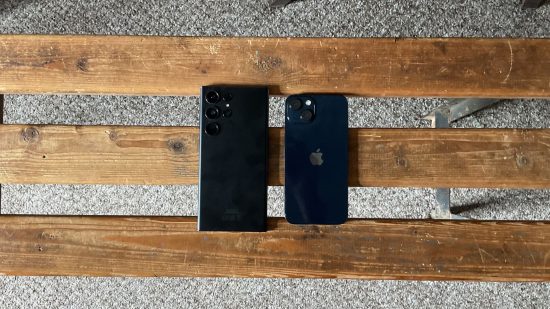 iPhone vs. Samsung: which is better for gaming? header image showing two phones, the iPhone 13 and the Samsung S23 Ultra. They're both black, showing their backs lying on their screens on a bench.