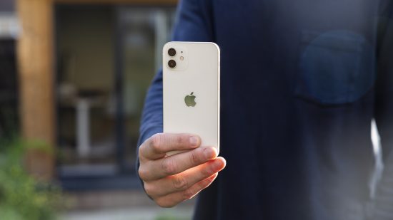 A white iPhone 12 being held in a man's hands outside