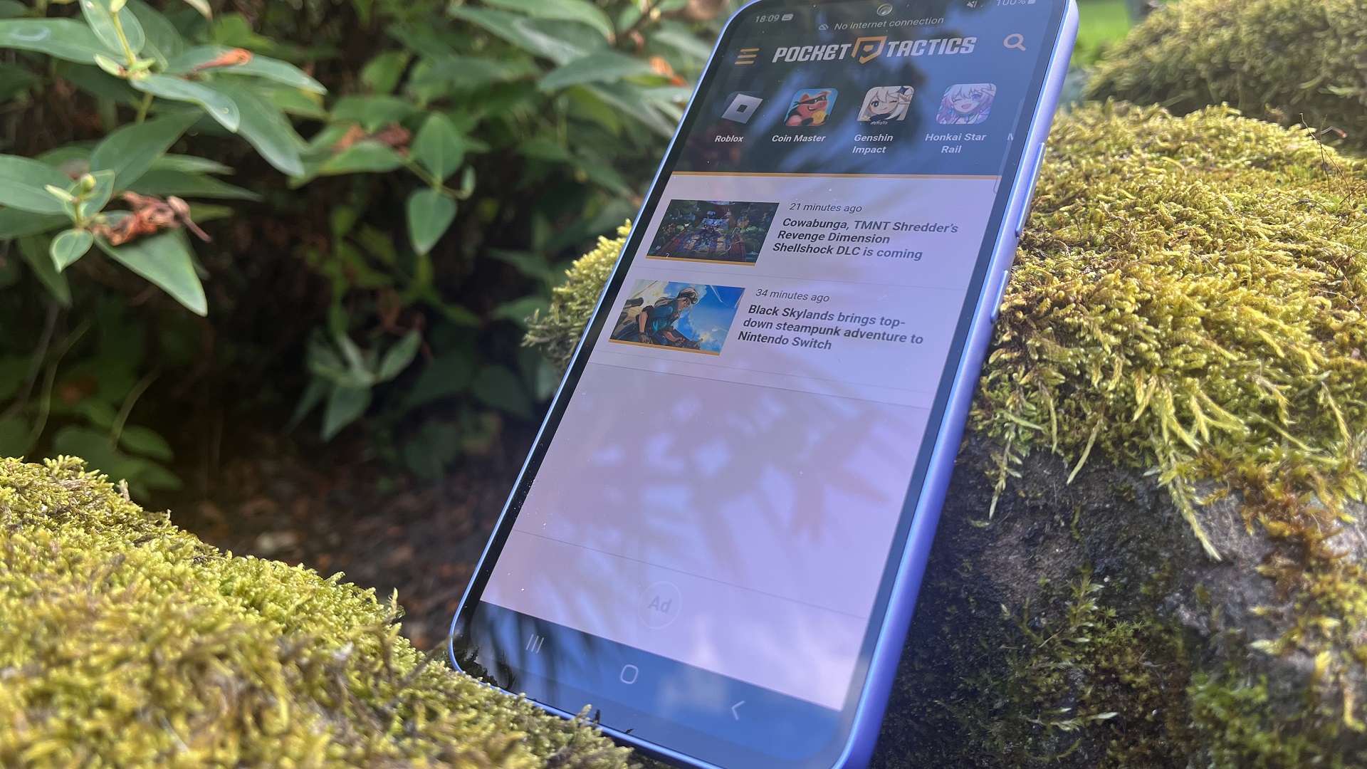 Recenzja Samsunga A54 - telefon stojący na omszałej skale z wyświetloną na ekranie stroną Pocket Tactics