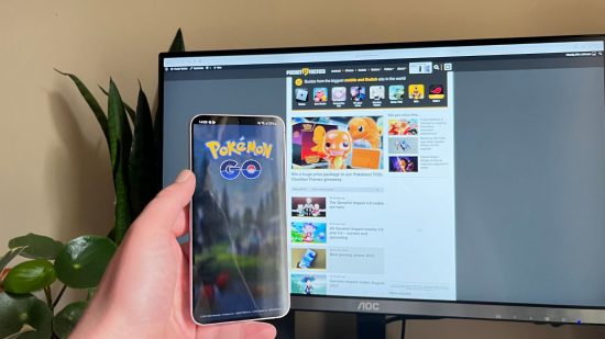 Samsung Galaxy S23 review shot showing the Samsung Galaxy S23, in Lavender, showing its screen playing Pokemon Go in front of a blurred monitor.