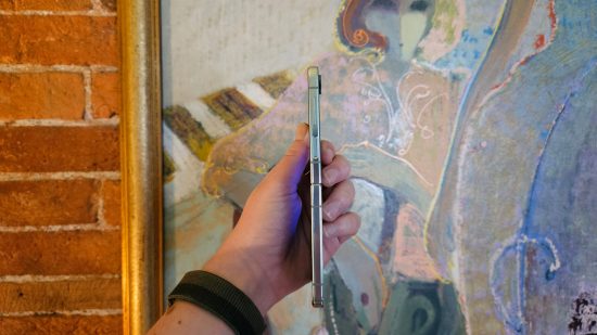 Samsung Galaxy Z Flip5 header showing the phone unfolded flat held in a hand side-on in front of an abstract picture of a woman.