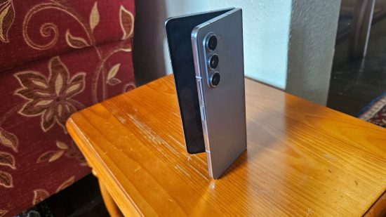 Samsung Galaxy Z Fold5 review header showing the phone in blue half folded standing upright on a wooden table with the three cameras showing.