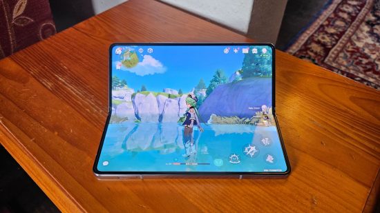 Samsung Galaxy Z Fold5 review header showing the phone in blue half folded standing upright on a wooden table with the inner screen showing Genshin Impact..
