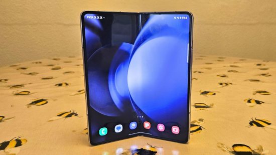 Samsung Galaxy Z Fold5 review header showing the phone in blue half folded standing upright on a wooden table with the large inner screen showing.