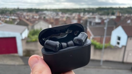 Razer Hammerhead Pro HyperSpeed review: a hand holds a pair of black earbuds in their charging case up in the street