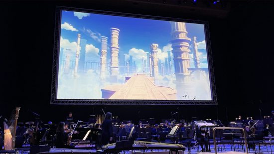 Genshin Concert 2024 - a photograph of the orchestra preparing as the load screen path plays on a projector screen