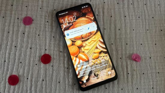 Custom image for Poco C65 review with the phone on a plain background showing an autumnal display on the lock screen
