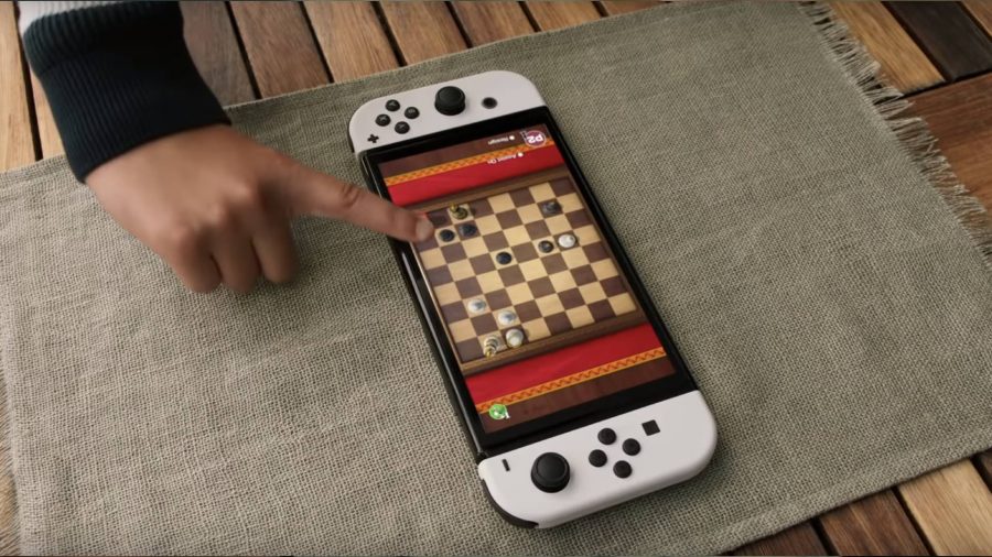 Two people are playing chess on the screen of a white Nintendo Switch OLED Model