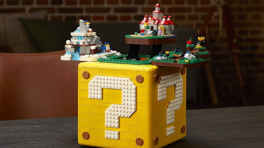 A Super Mario Question Block is made out of Lego, and it has been opened to reveal a diorama of small recreations of levels from Super Mario 64